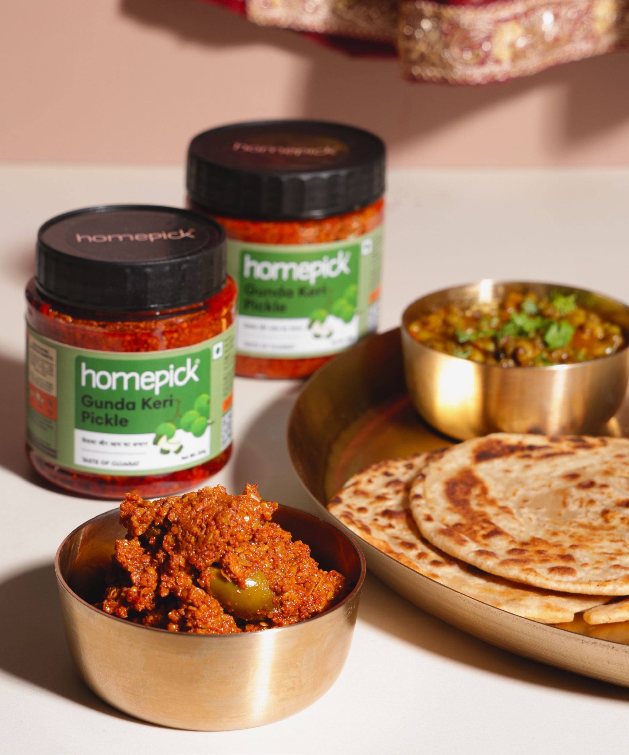 Homepick gunda keri pickles with a dish of food and hot paratha & chana on a table.