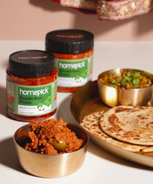 Homepick gunda keri pickles with a dish of food and hot paratha & chana on a table.